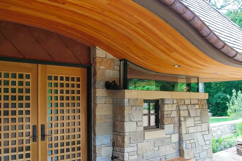 Entry with gridded wood double doors, copper diamond cladding, stone walls and a sweeping curved wood soffit