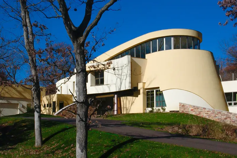 Sculptural cream stucco house with sweeping curved walls and a curved band of clerestory windows under a blue sky