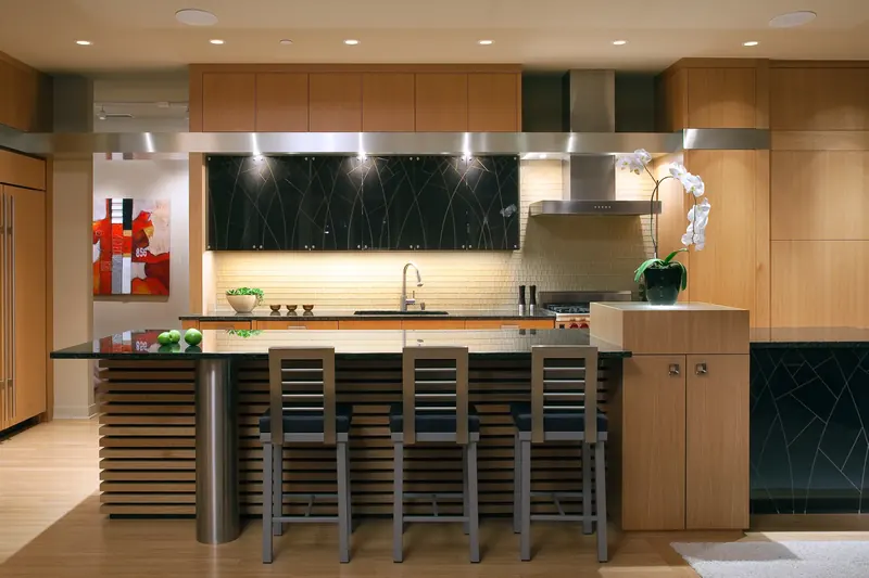 Warm wood kitchen with black geometric-patterned glass cabinets, slatted island base, stainless column and three bar stools