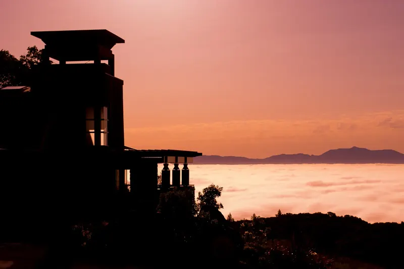 Silhouette of a stone tower home with a pergola-topped tower against a pink sunrise over a sea of fog