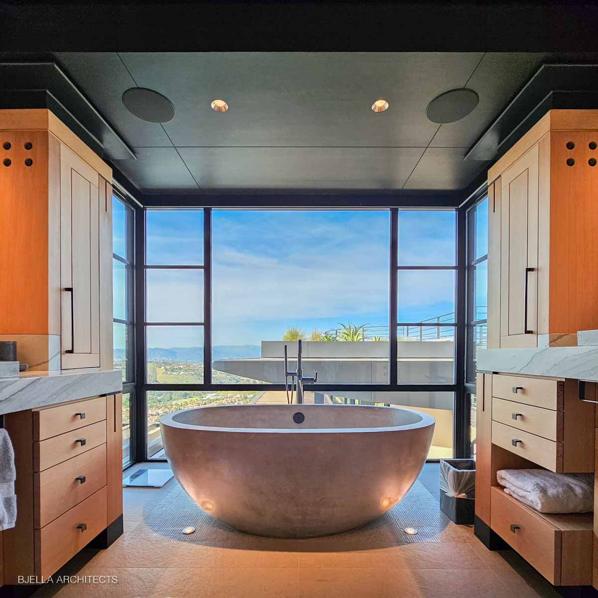 Freestanding stone tub facing a wall of glass
