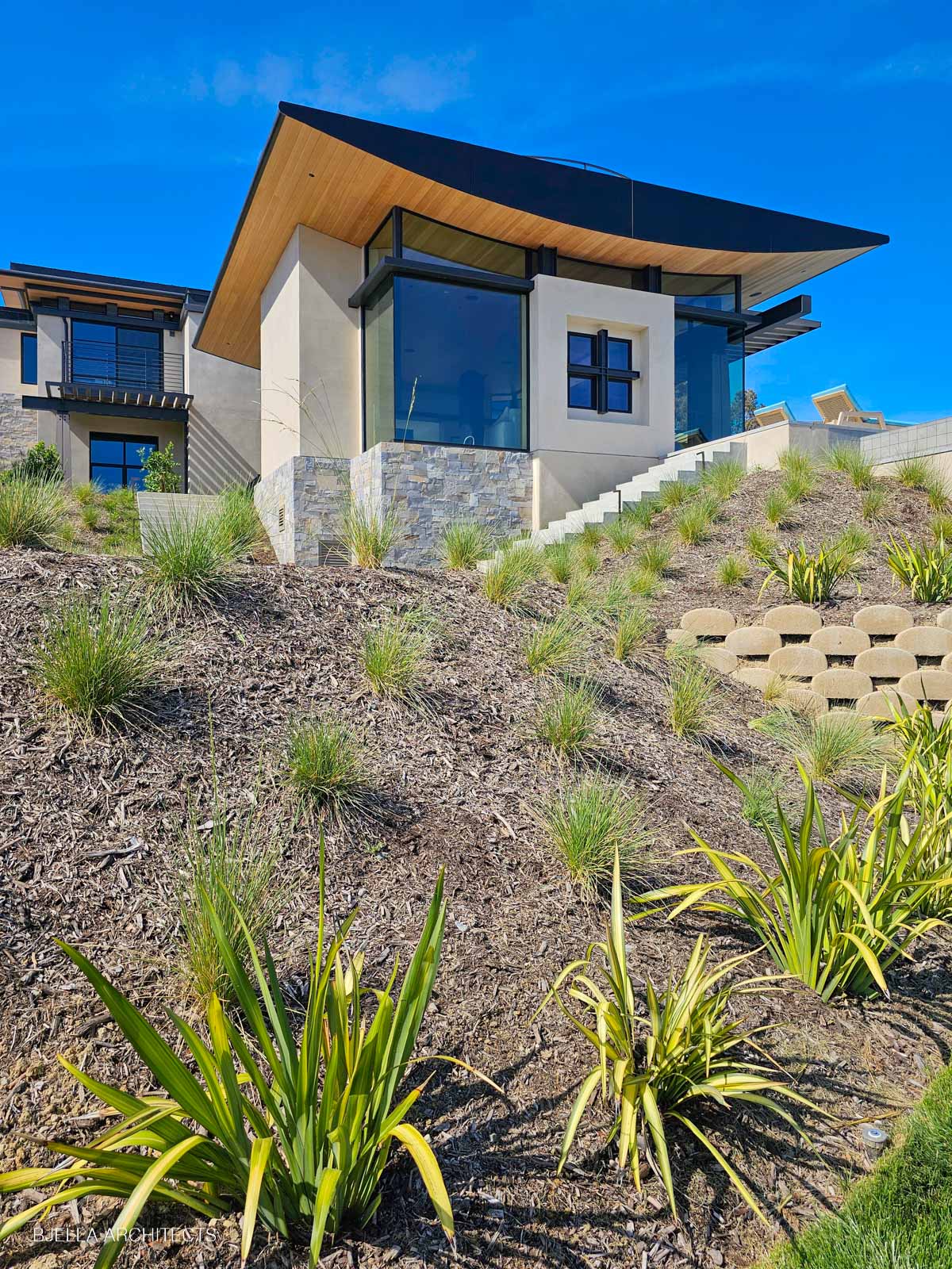 The house rising above the planted hillside on its stone base