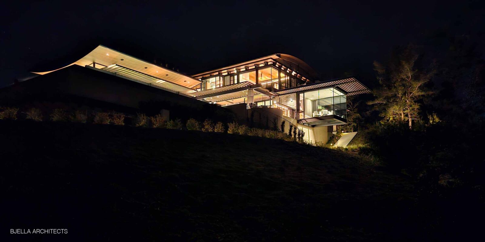 The house glowing against dark hills at night