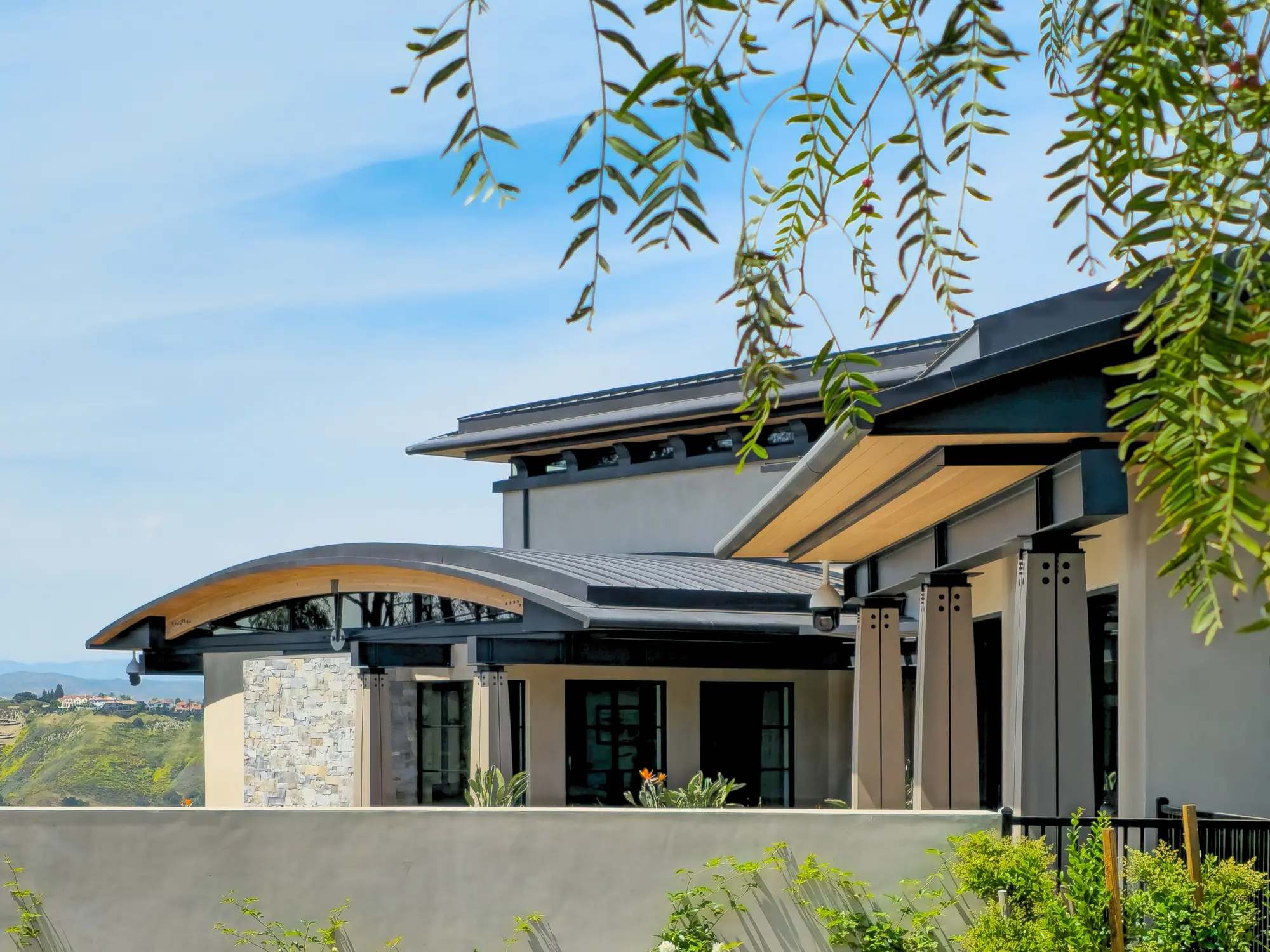 Curved metal roof with wood soffit and clerestory glass over bolted columns, with hills in the distance