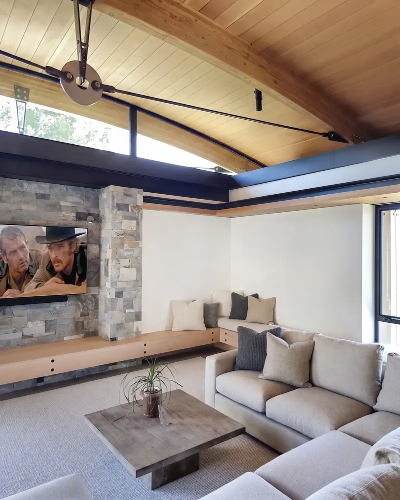 Family room with arched wood-paneled ceiling, steel tension rod, clerestory windows and a stone wall framing the TV