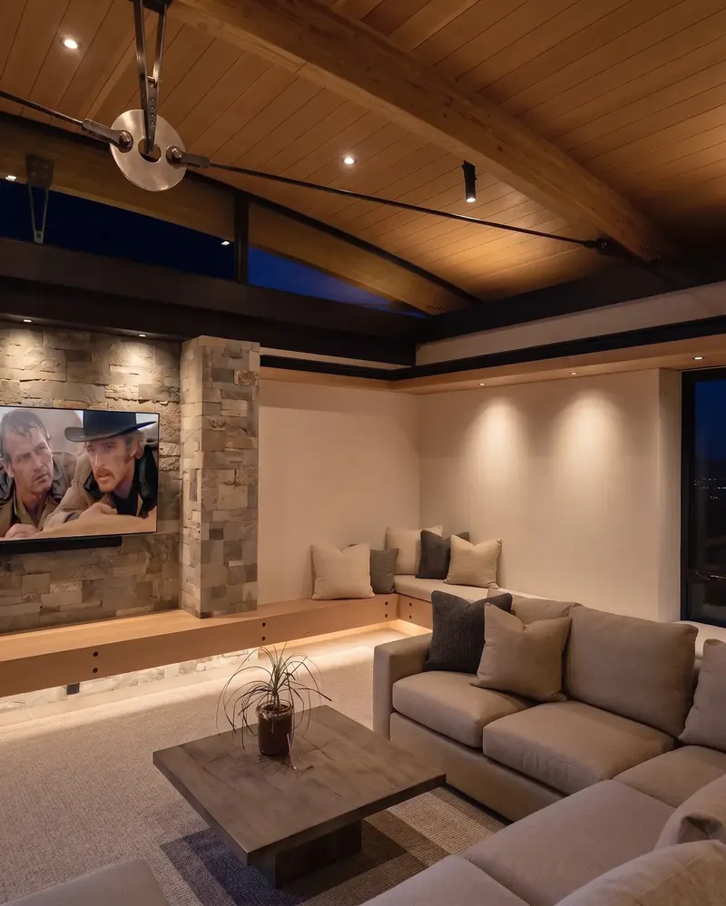 Family room at night with warm light on the arched wood ceiling, stone TV wall and built-in bench seating