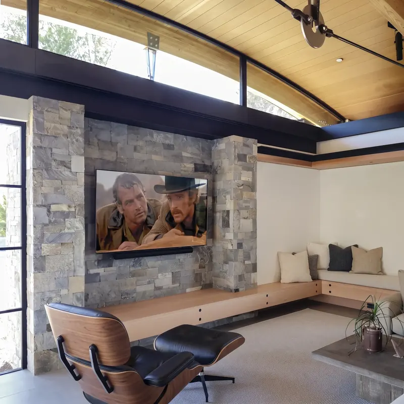 Lounge chair facing a stone-clad TV wall and built-in wood bench beneath an arched ceiling and clerestory windows