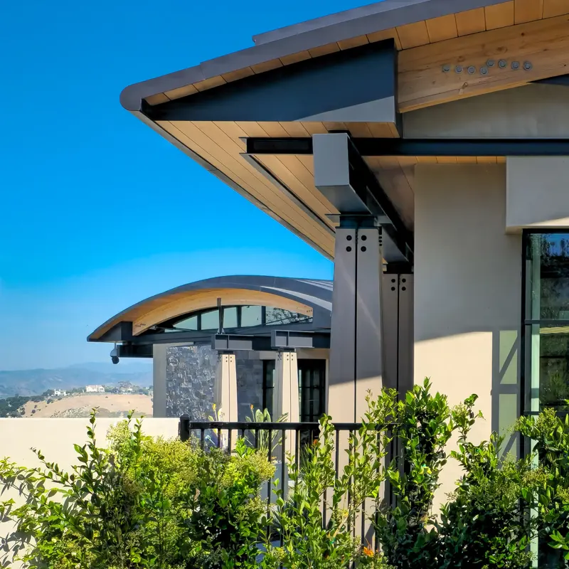 Deep wood soffit on steel beams and bolted columns, with an arched roof and dry hills beyond
