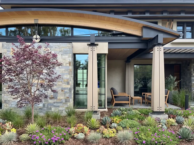 Covered patio with outdoor seating under a wood arch and tension rod, beside a stone wall and succulent garden