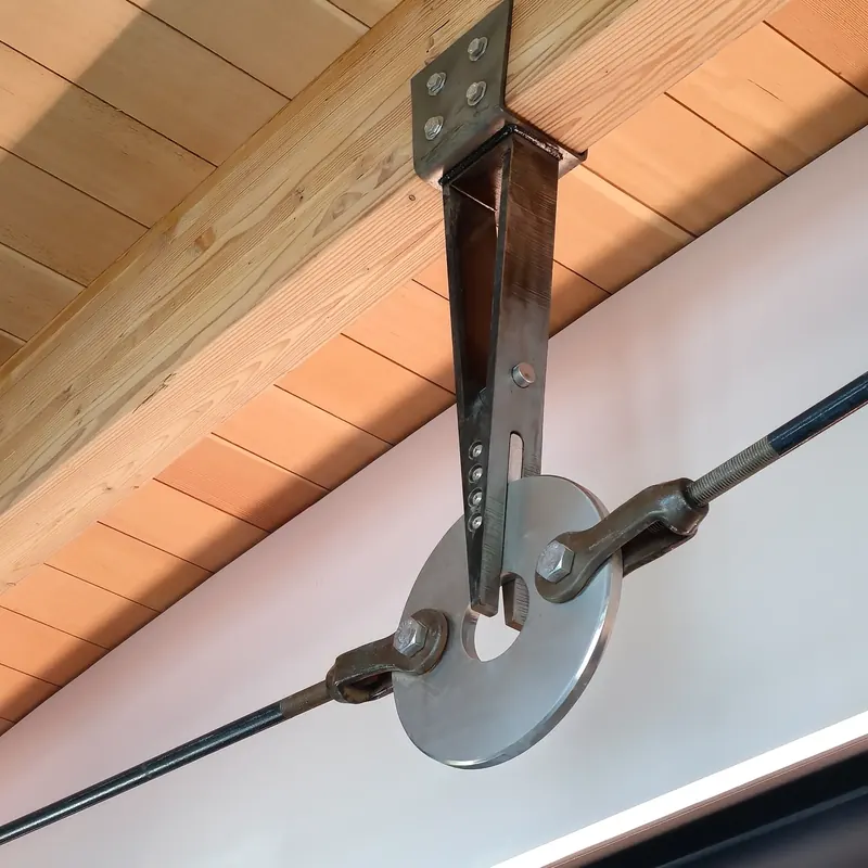 Custom steel bracket and ring joining tension rods beneath a wood beam and paneled ceiling