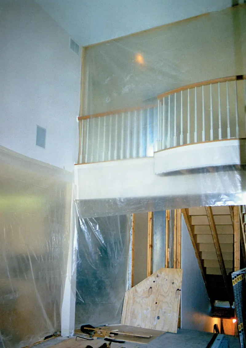 Balcony before remodeling, with spindle railing, plastic sheeting, plywood and a bare staircase below