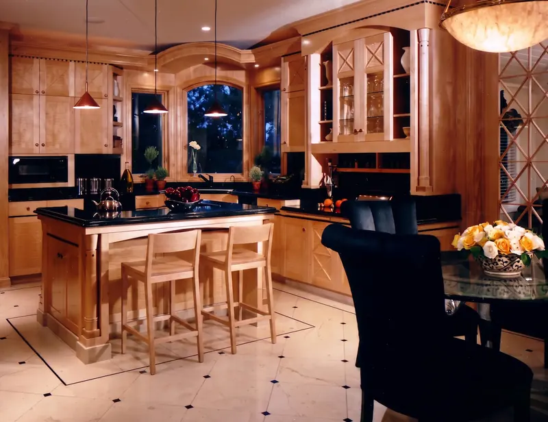 Kitchen after remodeling: figured-wood cabinetry, black counters, arched window at dusk and an island with two stools