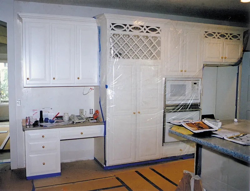 Kitchen desk before remodeling: white cabinets and wall ovens wrapped in plastic during construction