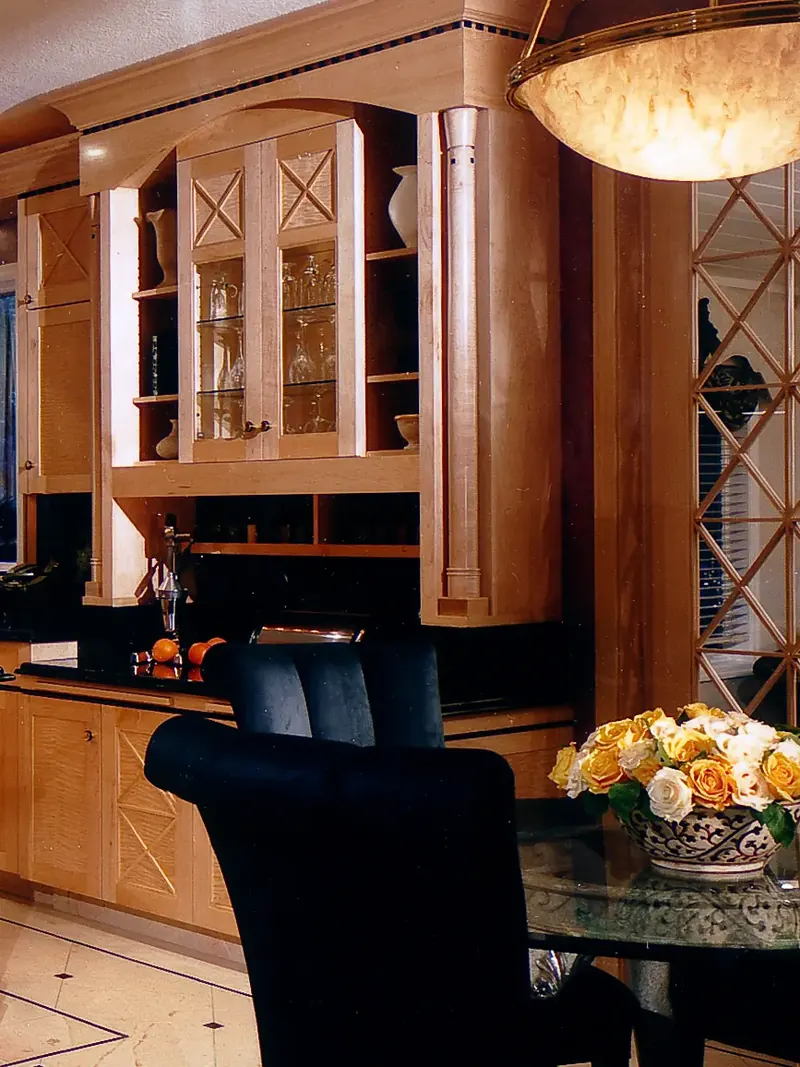 Glass-front display cabinet with stemware above a black counter, beside a glass table with roses