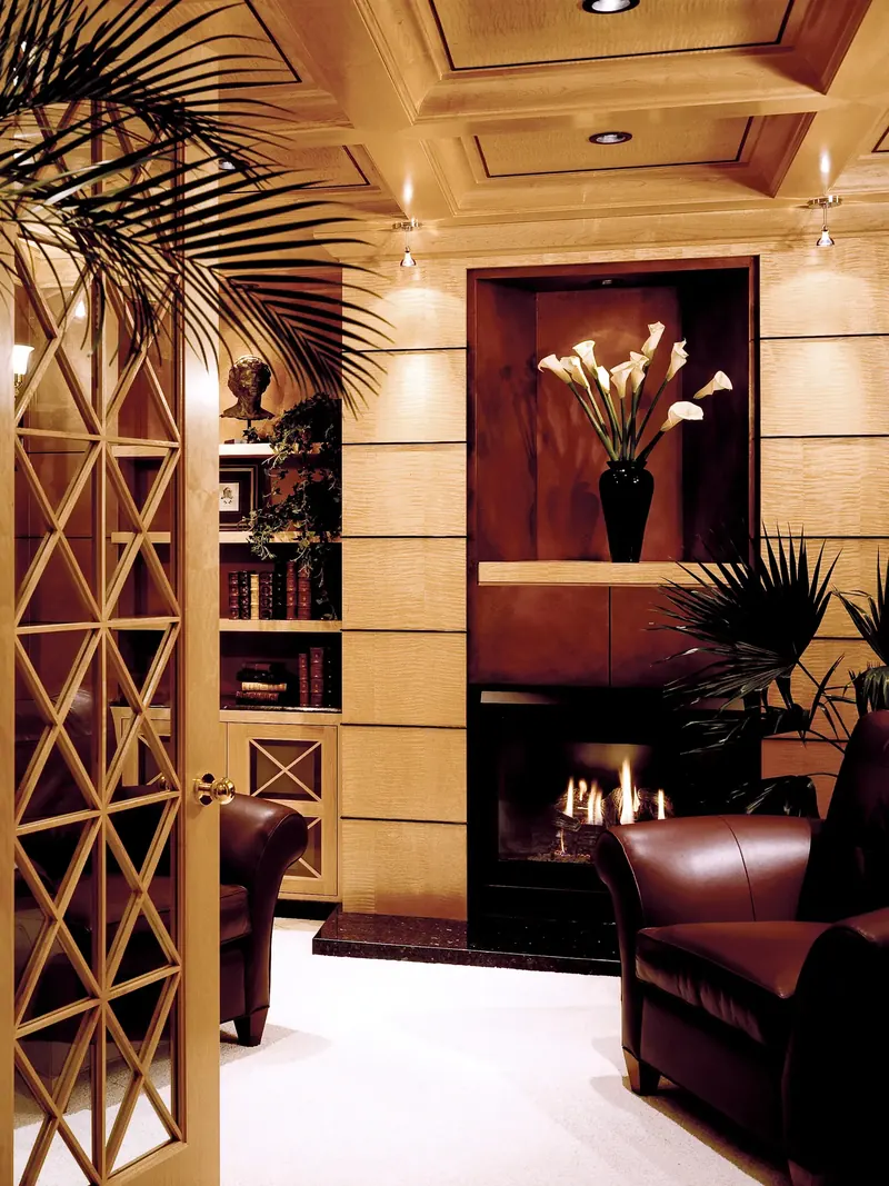 Library with wood-paneled walls, coffered ceiling, calla lilies in a niche above the fireplace and leather armchairs