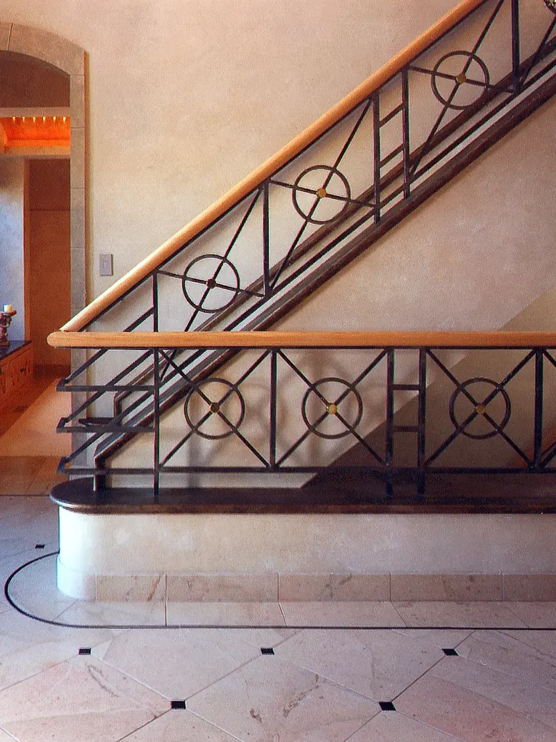 Close view of the iron stair railing with circle and cross motifs, wood handrail and curved plinth on a tile floor