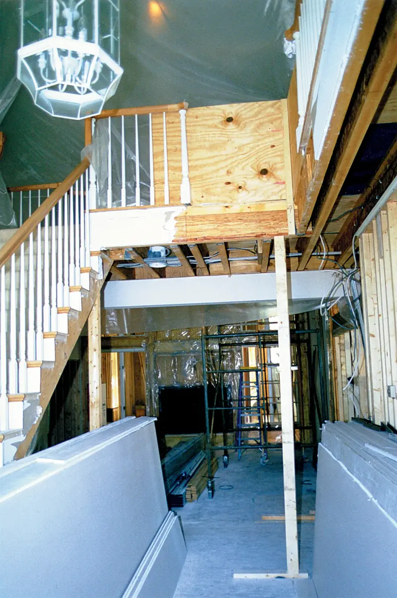 Stairway before remodeling, mid-construction with spindle railing, exposed joists, scaffolding and stacked drywall