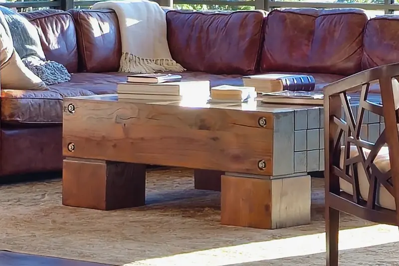 Rugged wood beam coffee table with bolted joints and block legs, in front of a leather sectional sofa