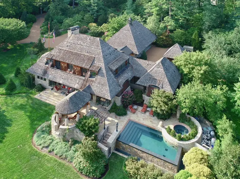 Aerial view of the shingled hip roofs, round dining pavilion, pool and spa set among mature trees
