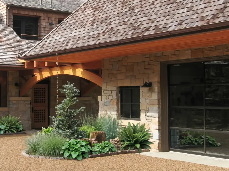 Arched timber porte-cochere beside a stone garage wall, with a lattice wood door and a planted bed