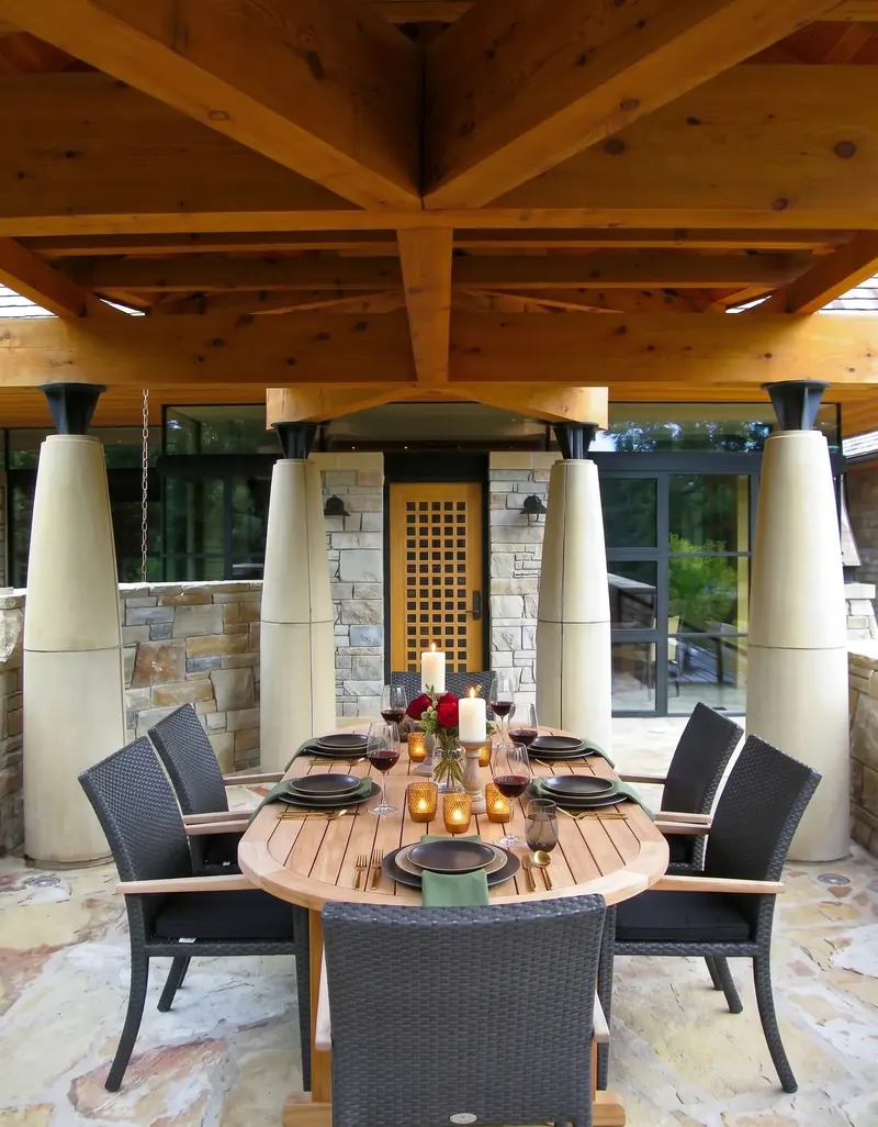Outdoor dining pavilion with layered exposed timber beams on tapered columns over a set wood table