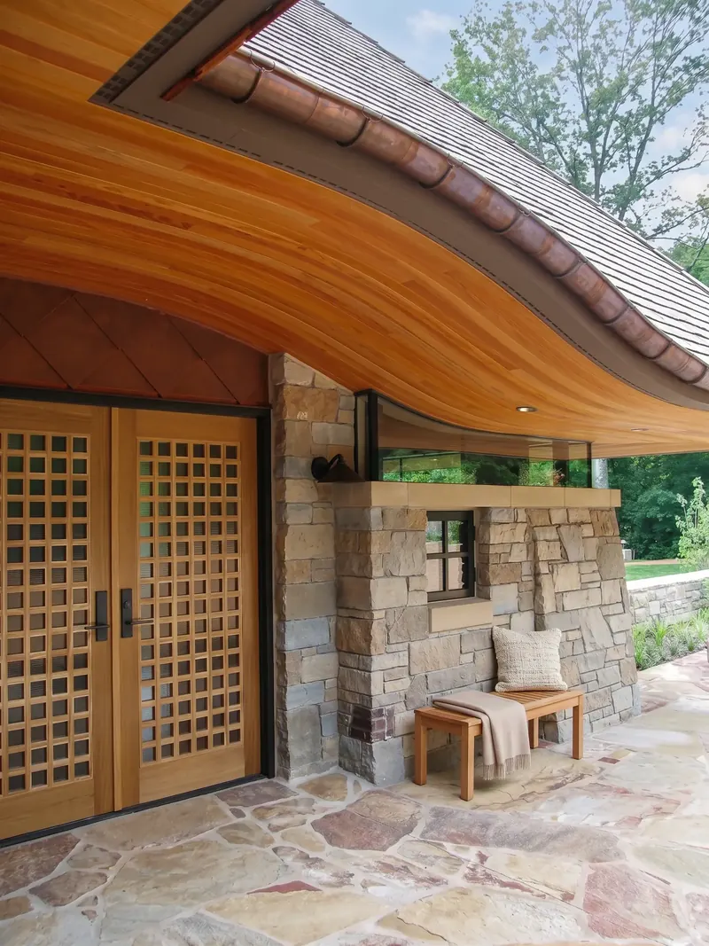 Lattice wood entry doors beneath a curving wood soffit, with a band of glass separating the roof from the stone wall