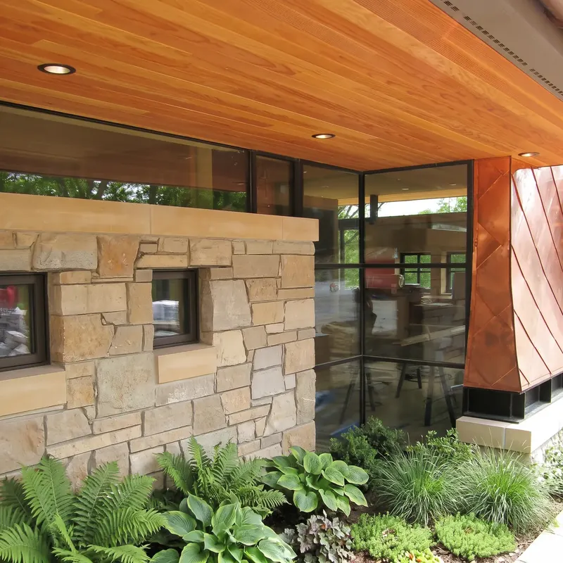 Wood soffit floating over a ribbon of glass atop a stone wall, meeting a flared copper-clad corner