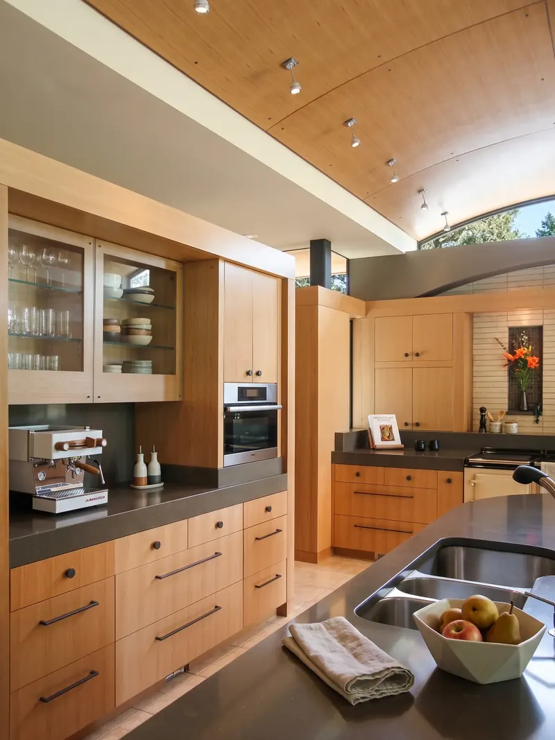 Kitchen with an arched wood ceiling, wood cabinetry, glass-front cupboards and a dark-topped island with sink