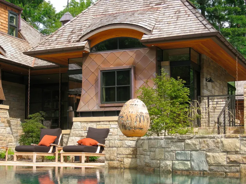 Copper fish-scale panels and arched clerestory above lounge chairs and an egg-shaped sculpture at the pool edge