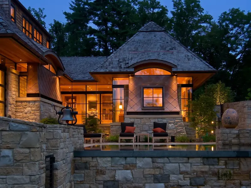 Copper Clad Eclectic Home at dusk, a copper-clad wing glowing above a stone-walled pool terrace