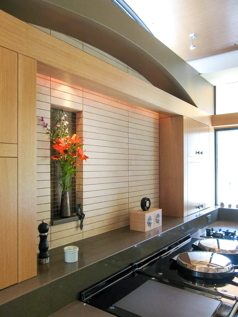Tiled backsplash with a recessed flower niche holding orange lilies behind the stove, under a curved soffit
