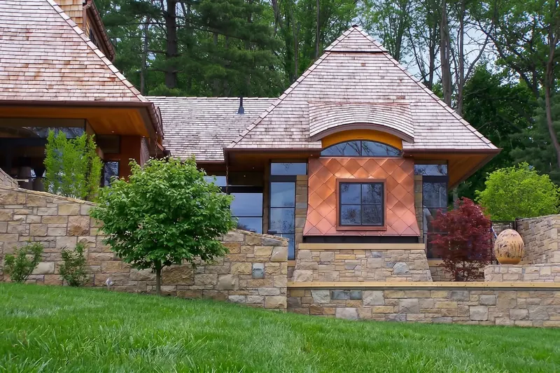 Pyramid-roofed wing with diamond copper panels and an arched window above sloping stone garden walls