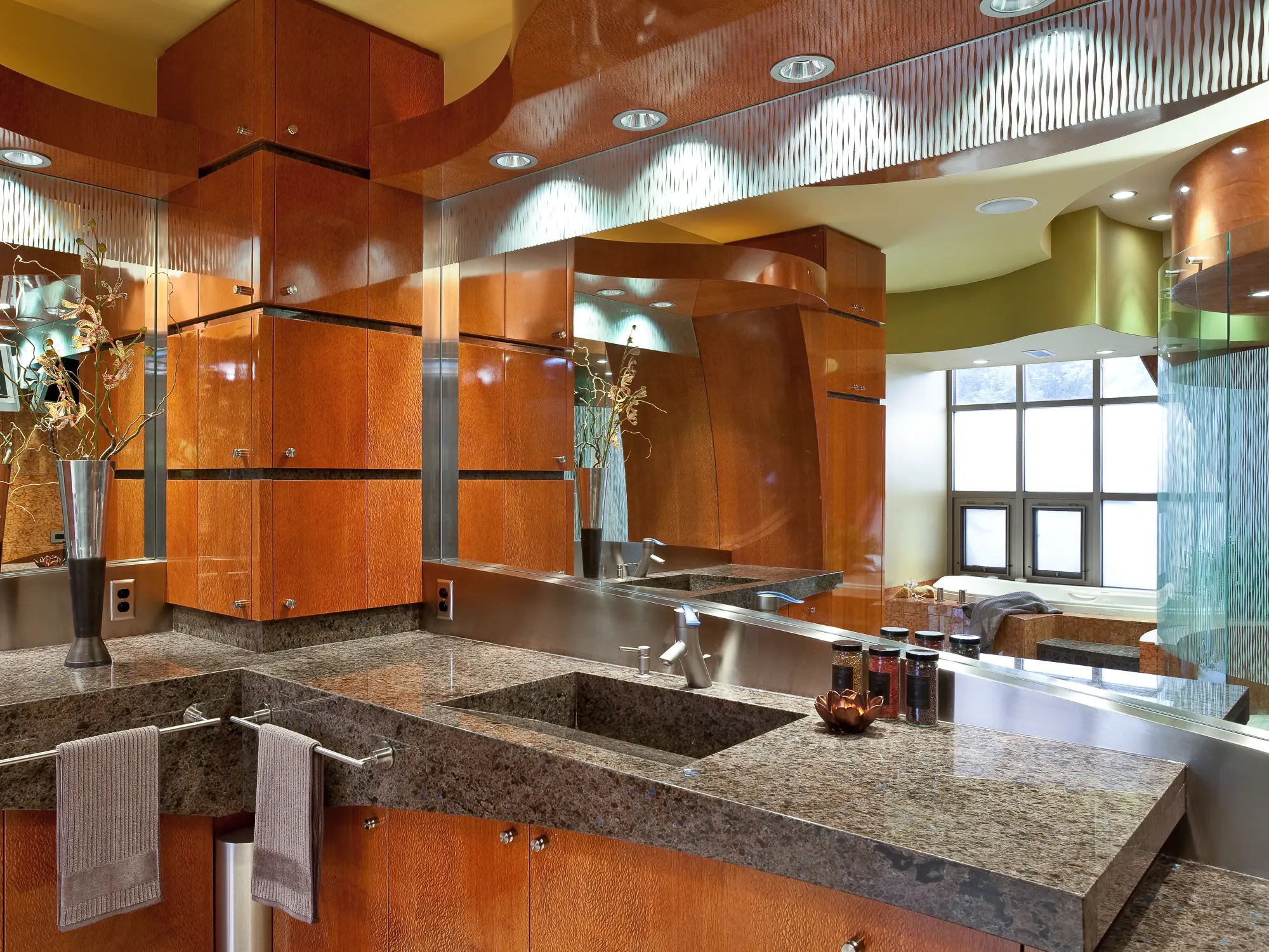 Bath vanity with an integral stone sink, figured wood cabinets and a mirror reflecting the tub