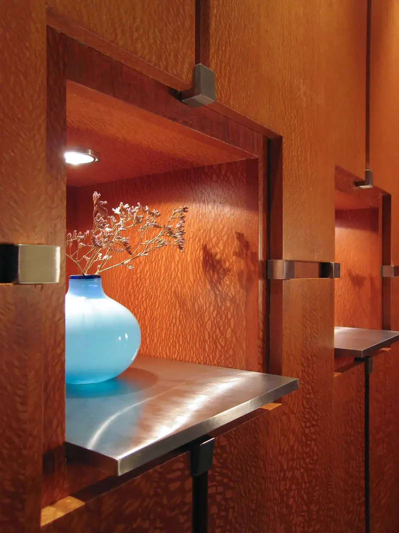 Close-up of a wood-lined niche with a stainless shelf and a turquoise glass vase of dried flowers