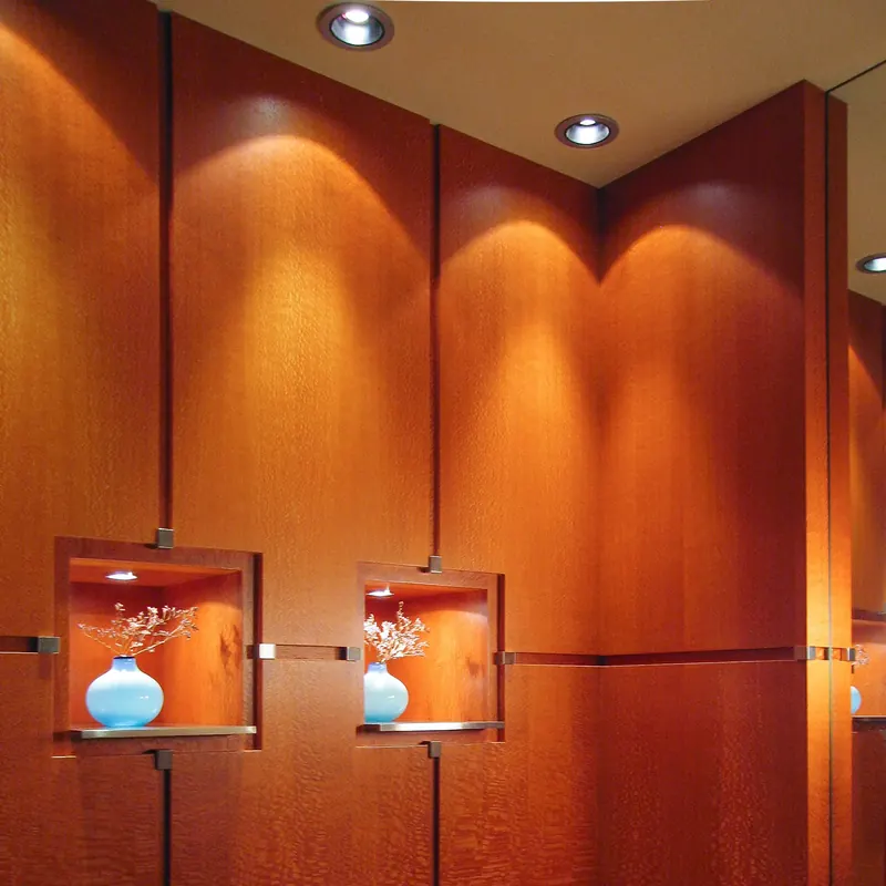 Figured wood wall panels with lit display niches holding pale blue glass vases