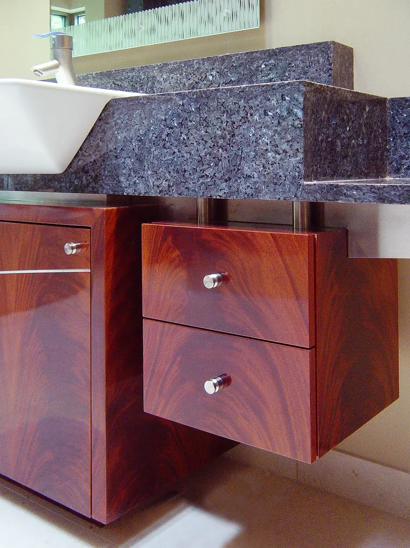 Detail of floating mahogany drawers beneath a thick blue-grey stone vanity top and white sink