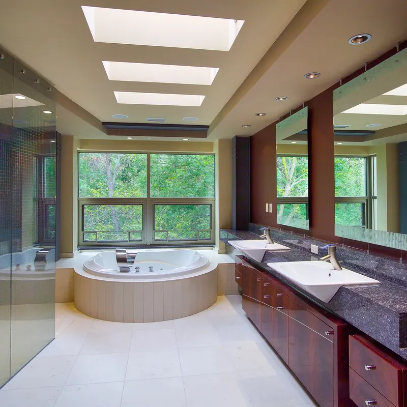 Bath with three skylights, a tiled tub before tall windows to the trees and a long double vanity