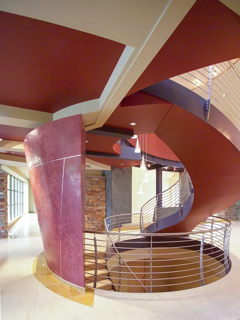 Tapered red plaster wall beside the stair opening, the stair spiraling up under red ceilings to the floor above