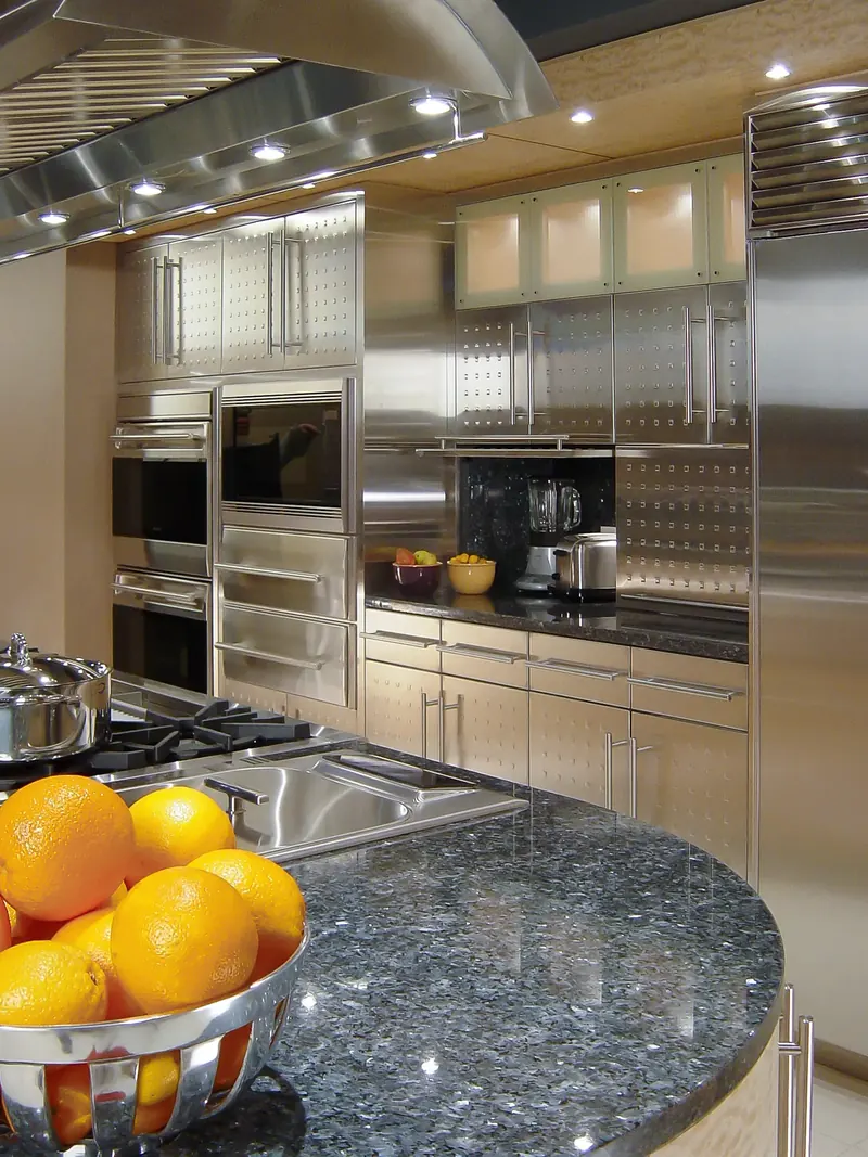 Stainless wall of ovens and cabinets with an open appliance garage, bowl of oranges in the foreground