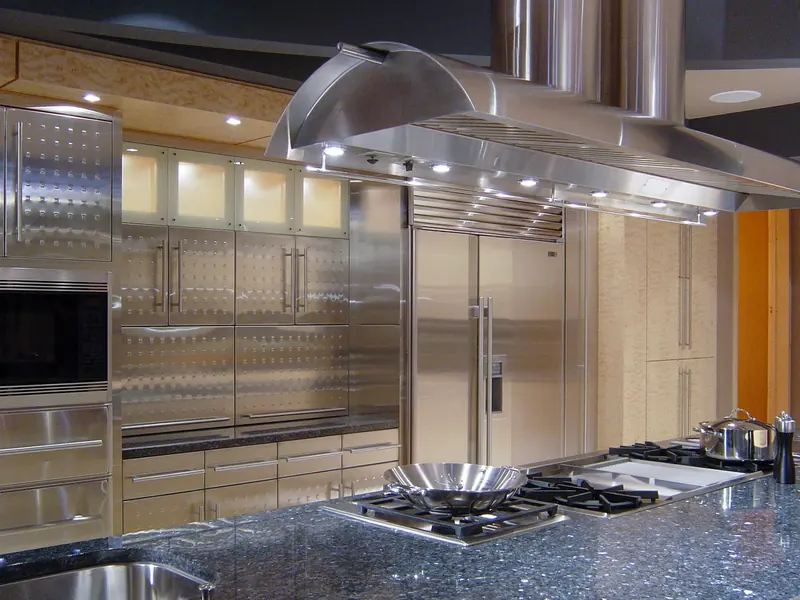 Wok and cooktops on a dark stone island beneath a long stainless vent hood