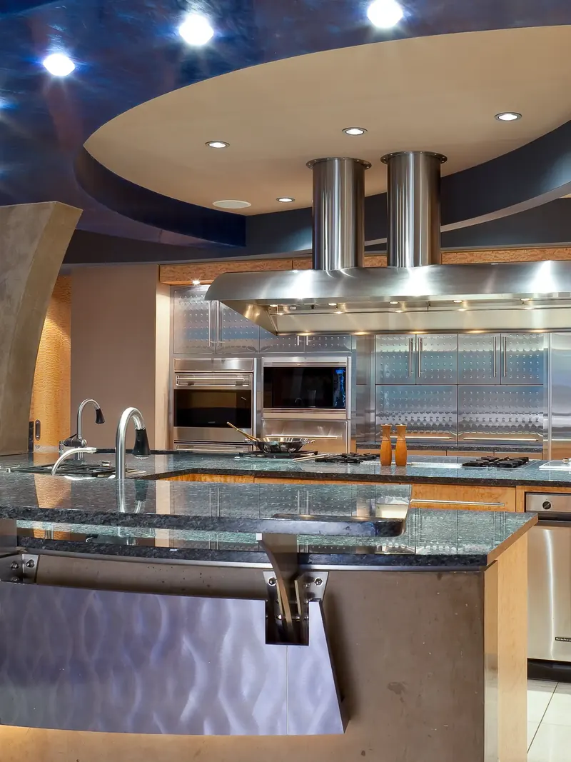 Island cooktops and prep sinks before a wall of patterned stainless cabinets, ovens and refrigeration