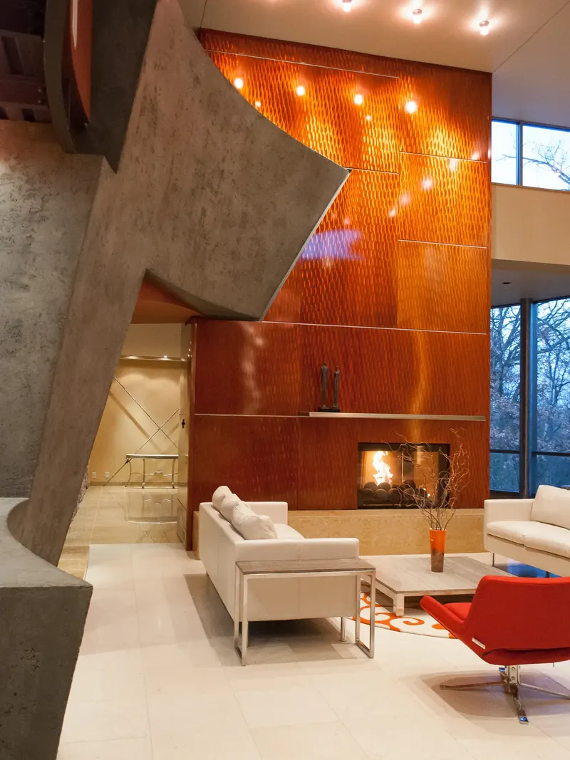 Grey plaster bridge structure angling past a two-story textured orange fireplace wall with a long steel mantel