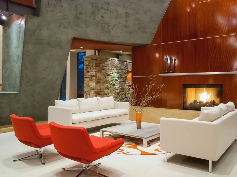 Living room with red swivel chairs and white sofas before a glossy orange fireplace wall and stacked stone