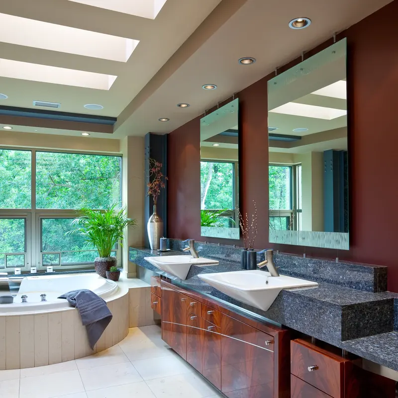 Mahogany vanity with angled white sinks and suspended mirrors on a deep red wall, tub and windows at left