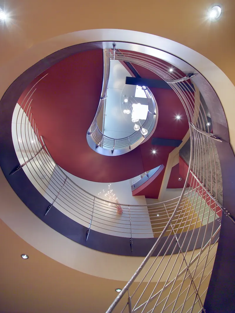 Looking straight up the stairwell: spiraling steel railings, red ceiling planes and a skylight with glass pendants