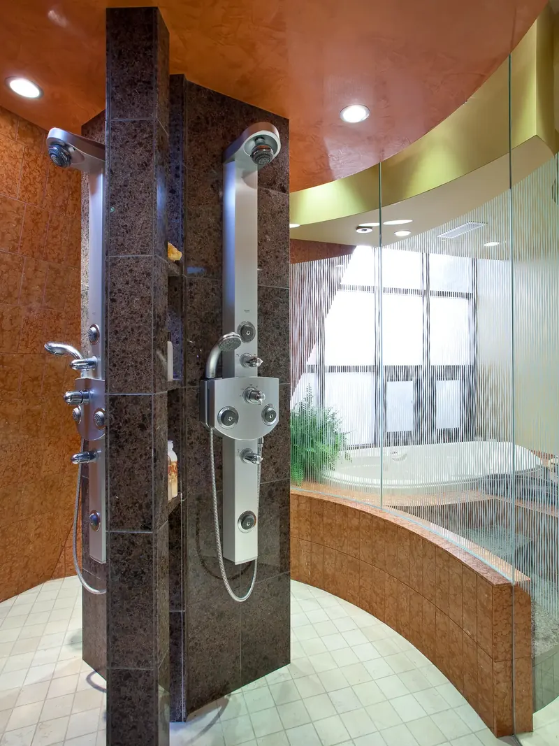 Shower with a dark stone column holding two stainless shower panels, curved glass wall beyond