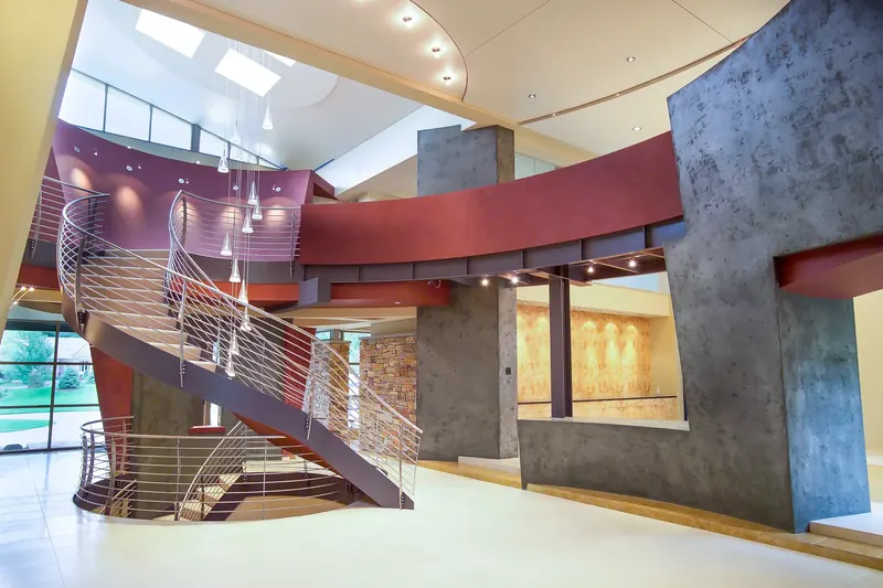 Two-story hall with the curving staircase, red bridge on steel beams, cone pendants and textured grey plaster walls
