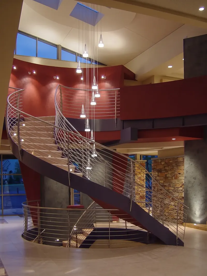 Curved staircase at evening, cascade of cone pendants against a red wall and stacked stone piers
