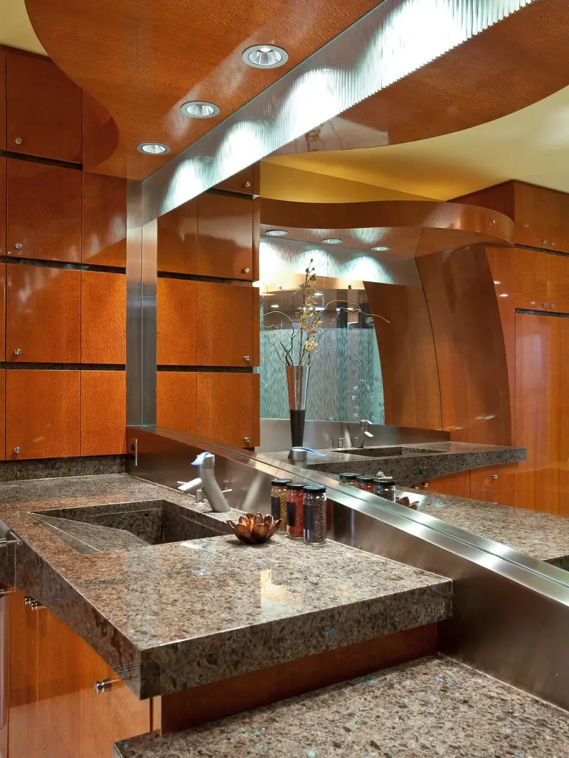 Thick stone counter with a sloped integral sink below a curved wood ceiling and long mirror