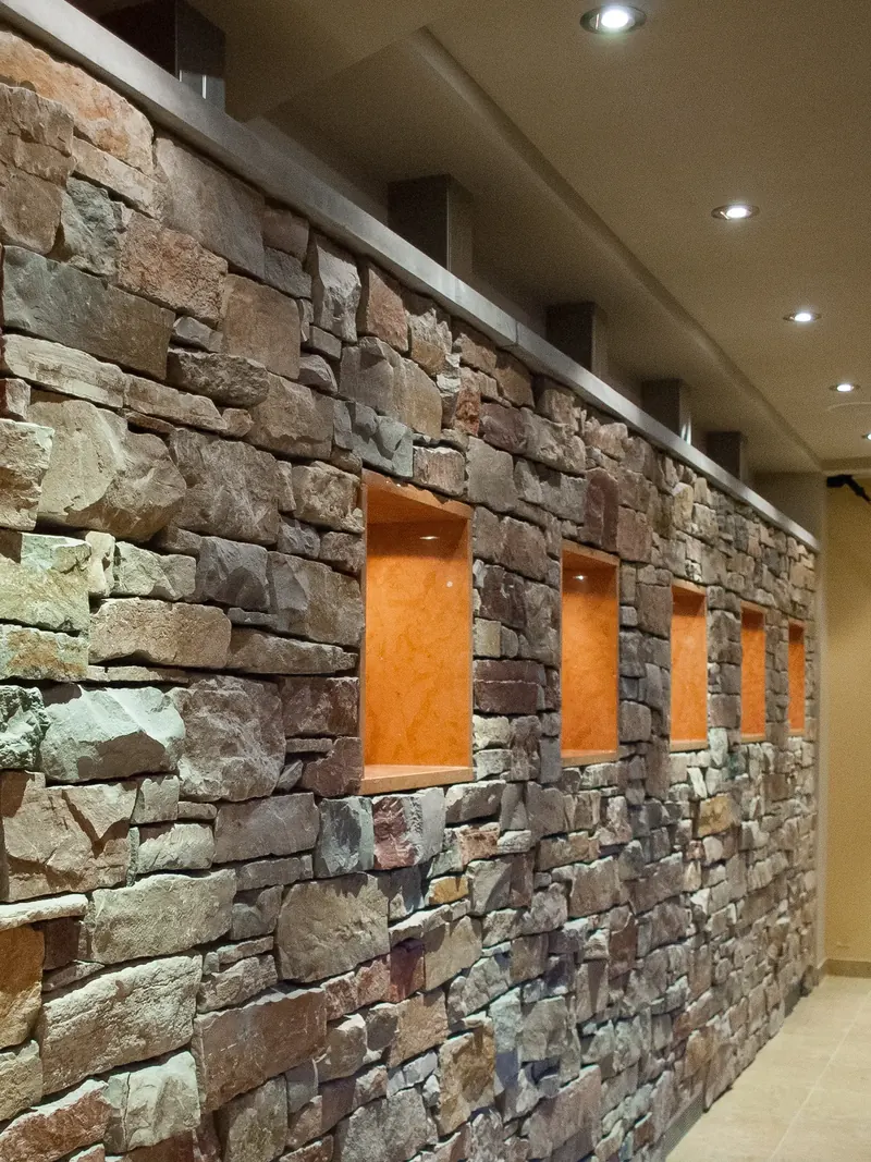 Multicolored stacked stone wall with a row of recessed orange niches and a steel cap
